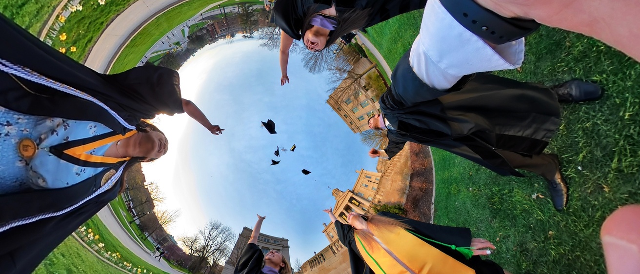 Graduates throwing caps in air in front of Old Cap